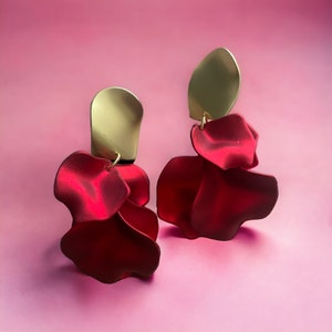 May include: A pair of red flower-shaped earrings with gold accents. The earrings are made of fabric and have a delicate, feminine look.