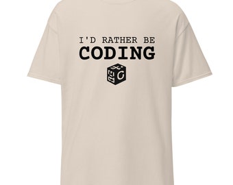 Può includere: Una maglietta beige con il testo "I'd rather be coding" in nero. Sotto il testo c'è un cubo bianco e nero con la lettera "C" all'interno.