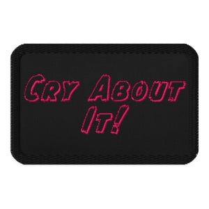 Op de afbeelding: Zwarte geborduurde patch met roze opschrift "Cry About It!"