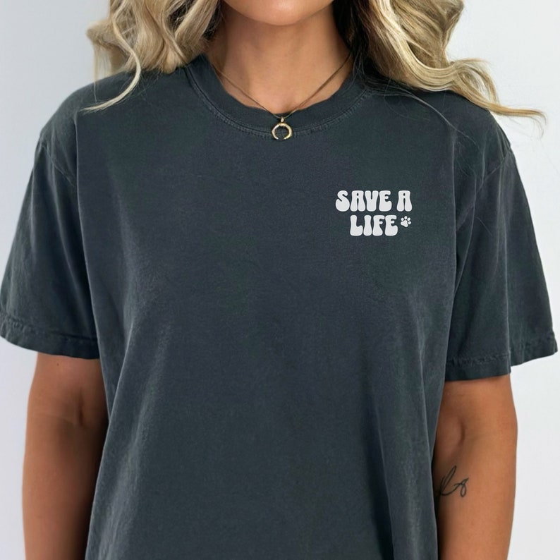 May include: A dark gray t-shirt with the text "SAVE A LIFE" in white with a paw print.