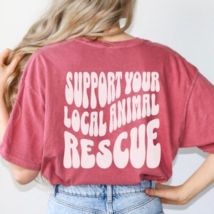 May include: A red t-shirt with the text "SUPPORT YOUR LOCAL ANIMAL RESCUE" in white, retro-style lettering.