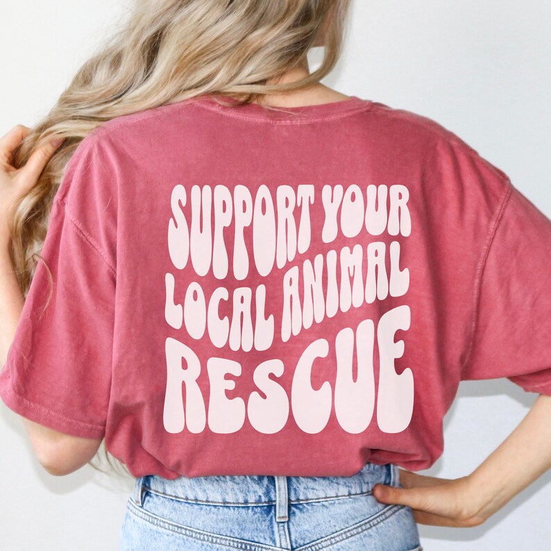 May include: A red t-shirt with the text "SUPPORT YOUR LOCAL ANIMAL RESCUE" in white, retro-style lettering.