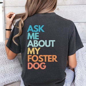 May include: A black t-shirt with the text "Ask Me About My Foster Dog" in a rainbow gradient.
