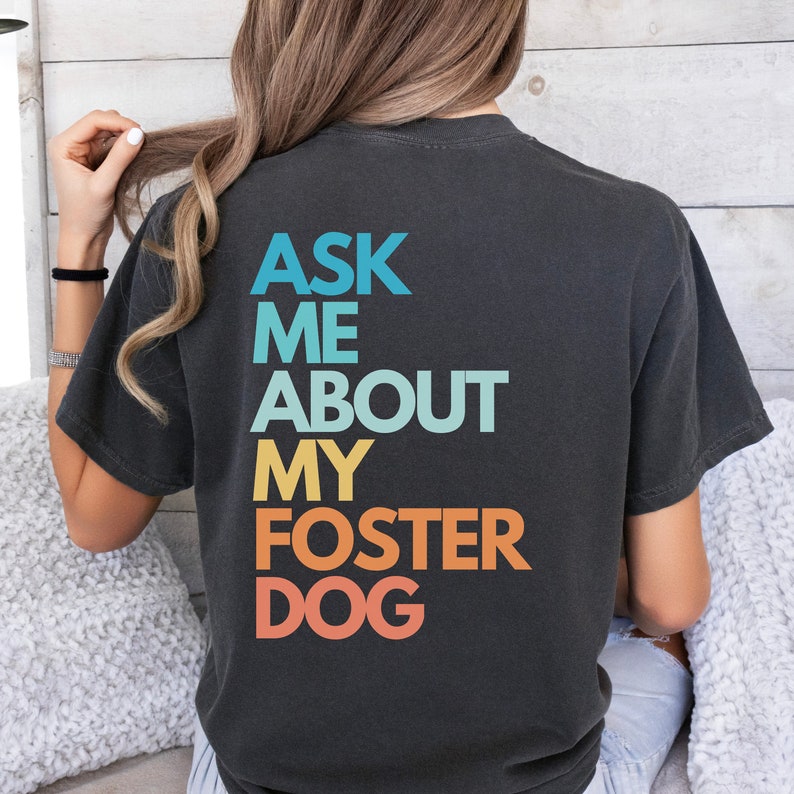 May include: A black t-shirt with the text "Ask Me About My Foster Dog" in a rainbow gradient.