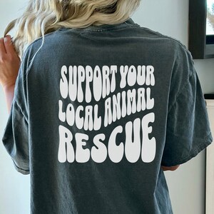 May include: A dark gray t-shirt with the text "SUPPORT YOUR LOCAL ANIMAL RESCUE" in white, retro-style lettering.