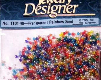 May include: A bag of transparent rainbow seed beads, weighing 0.705 ounces or 20 grams. The beads are small and round, and they are a mix of colors, including red, orange, yellow, green, blue, and purple.
