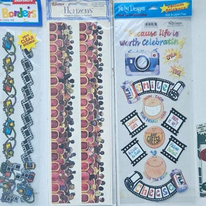 May include: Four sheets of stickers featuring film strip borders, a crowd of people, a camera with the text "Because life is worth celebrating", and a film strip with the text "Say Cheese".