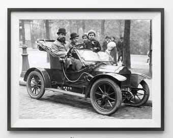 May include: Black and white framed print of a vintage car with passengers. The car has large spoked wheels and is driven by a man wearing a bowler hat. The print is labeled "l'amour Art Studio".