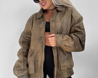 May include: A brown leather jacket with a collared neckline, two front pockets, and a zipper closure. The jacket has a slightly distressed appearance and a relaxed fit. The sleeves are gathered at the cuffs.