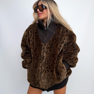 May include: A brown and black leopard print faux fur jacket featuring a dark brown ribbed knit high collar, long sleeves with ribbed cuffs, and a full-length front zipper closure. The jacket has a thick, textured pile and a relaxed fit.