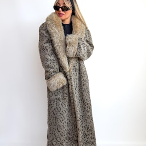 May include: A long, patterned coat with a faux fur collar and cuffs. The coat features a leopard print design in shades of gray and brown. The coat is floor-length and has a wrap-style closure.