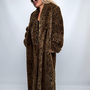 Può includere: Un cappotto lungo in pelliccia sintetica che arriva fino a terra, caratterizzato da una stampa animalier marrone scuro e nera. Il cappotto presenta un ampio colletto a revers, maniche lunghe e una silhouette dritta che arriva alle caviglie.