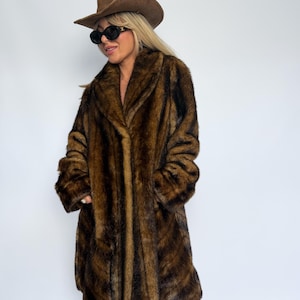 May include: A brown faux fur coat with a long-pile texture and dark brown vertical striping. The coat features a wide lapel collar and long sleeves. The ensemble includes a brown felt cowboy hat, black oval sunglasses, and leopard print trousers.