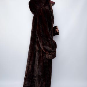 May include: A full-length, dark brown faux fur coat with a hood. The coat has long sleeves and a plush texture, creating a luxurious appearance. The coat is designed to provide warmth and coverage.