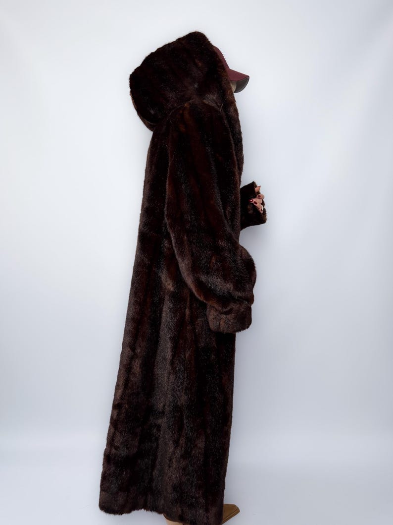 May include: A full-length, dark brown faux fur coat with a hood. The coat has long sleeves and a plush texture, creating a luxurious appearance. The coat is designed to provide warmth and coverage.