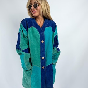 May include: A long-sleeved suede jacket featuring a color-blocked pattern in shades of royal blue, teal, and emerald green. The jacket has a V-neckline, a front button closure with three gold-toned circular buttons, and two side pockets.