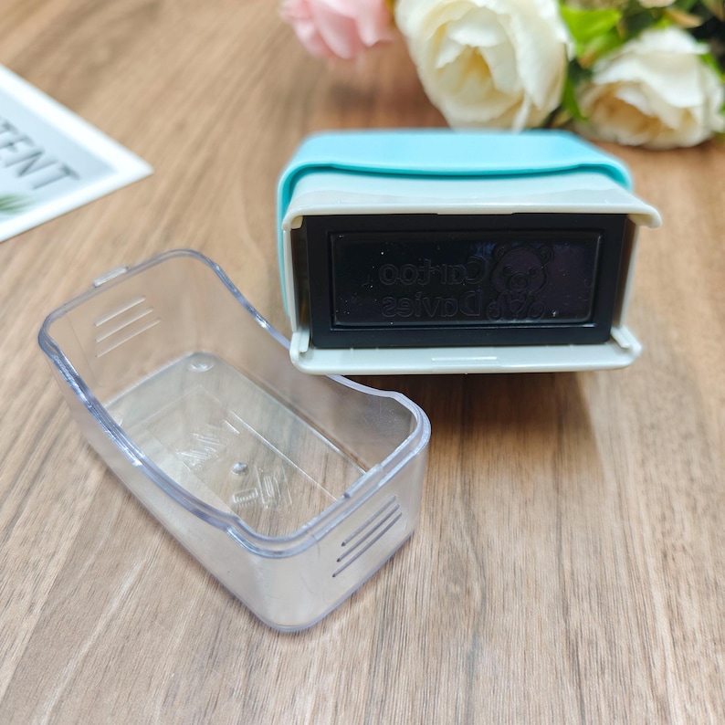 Puede incluir: Un sello autoentintable rectangular con una carcasa superior de color azul claro y una tapa protectora de pl&aacute;stico transparente. El mecanismo del sello presenta una cara rectangular negra con texto tenue y un peque&ntilde;o icono.