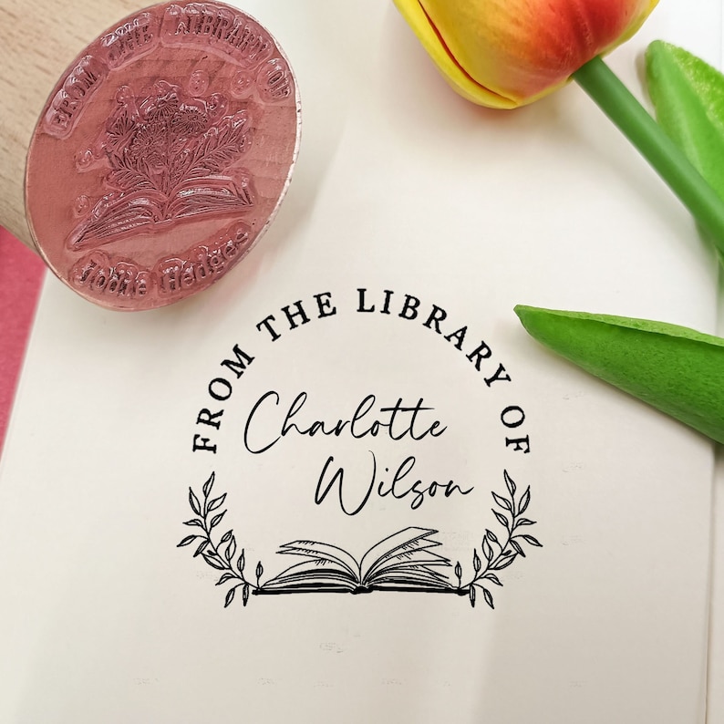 Peut inclure: Un tampon personnalis&eacute; avec l'inscription "FROM THE LIBRARY OF Charlotte Wilson" dans un cercle. Le design comprend une illustration de livre ouvert et des &eacute;l&eacute;ments floraux. Un second tampon indique "FROM THE LIBRARY OF Middle Hedges".