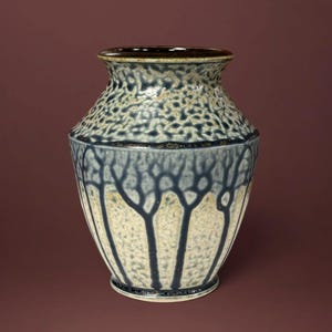 May include: A ceramic vase featuring a speckled cream and blue glaze. The upper section has a dense, mottled texture, while the lower body displays vertical, branching dark blue lines against a light, textured background with a dark rim.