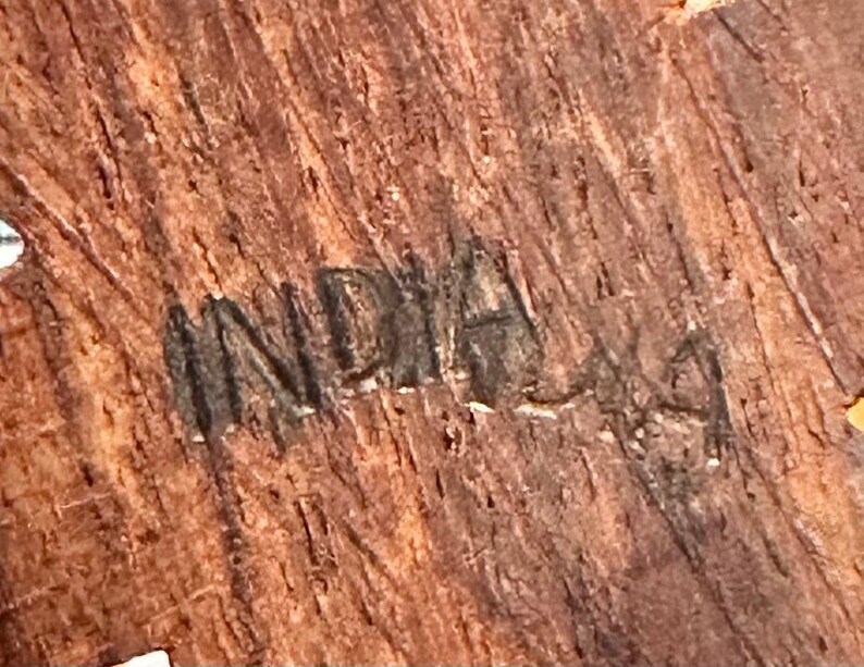 May include: A close-up view of a textured, brown wooden surface featuring the word INDIA stamped or burned into the grain. The wood displays a natural, fibrous pattern with vertical striations and dark brown tones throughout the material.