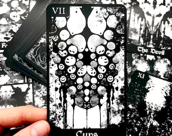 Peut inclure: Une carte de tarot noire et blanche avec le mot "Cups" en bas. La carte présente un motif central de cercles et de gouttes interconnectés, avec le chiffre romain VII en haut. D'autres cartes sont visibles en arrière-plan.