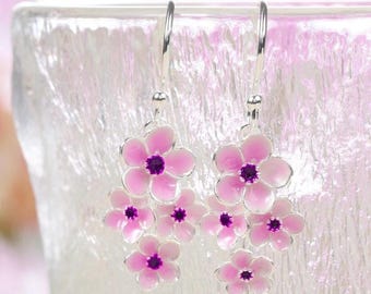 May include: Pink flower dangle earrings with purple crystal centers. The earrings are made of silver and have a delicate design.