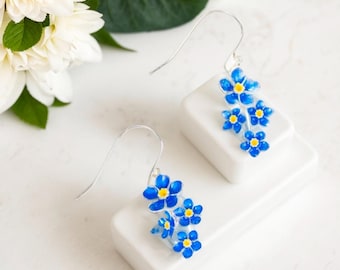 May include: A pair of silver dangle earrings with blue and yellow enamel forget-me-not flowers.
