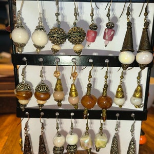 May include: A display of various earrings with different styles and colors, including white, brown, red, and green. The earrings are made of metal and glass beads.