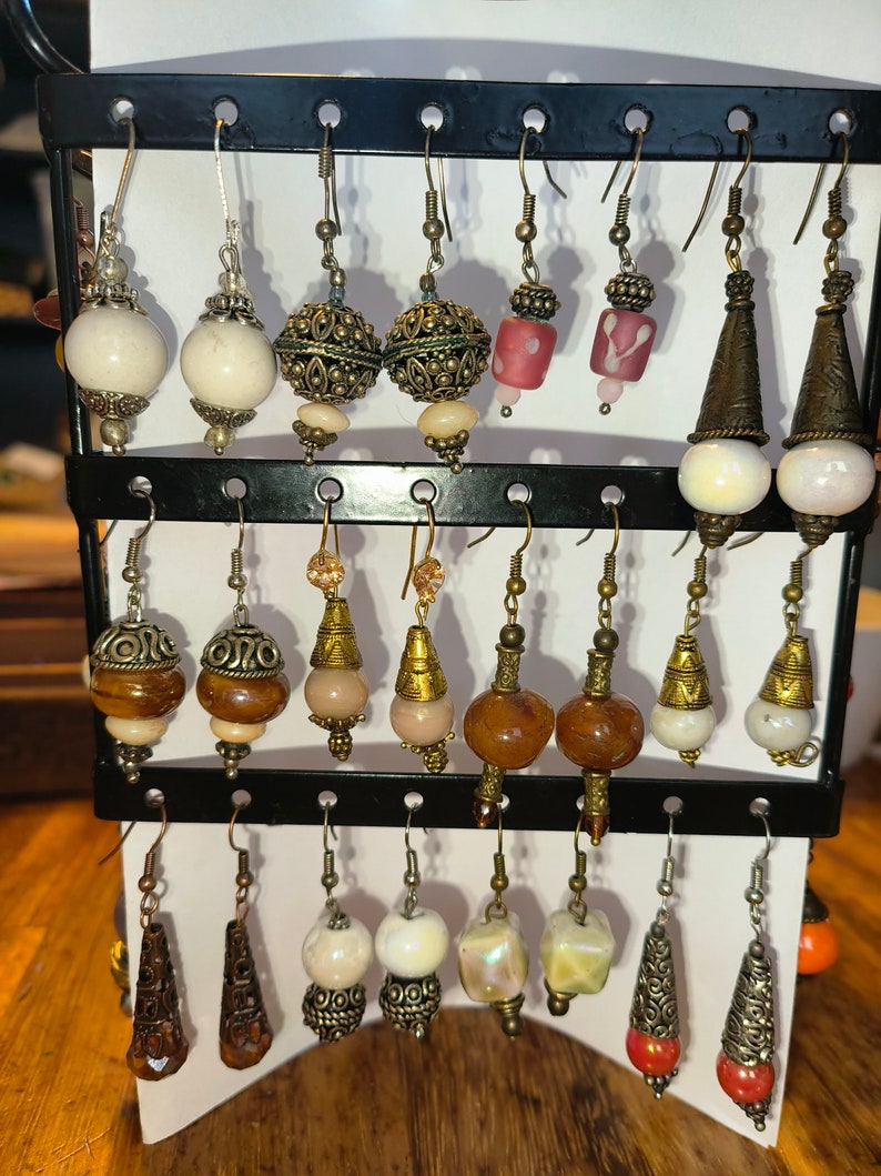 May include: A display of various earrings with different styles and colors, including white, brown, red, and green. The earrings are made of metal and glass beads.