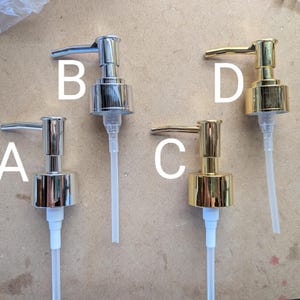May include: Four metal soap dispenser pumps in silver and gold tones. Two are silver, labeled A and B, and two are gold, labeled C and D. Each pump has a long, clear plastic tube for dispensing liquid. The pumps are designed for use with soap or lotion bottles.