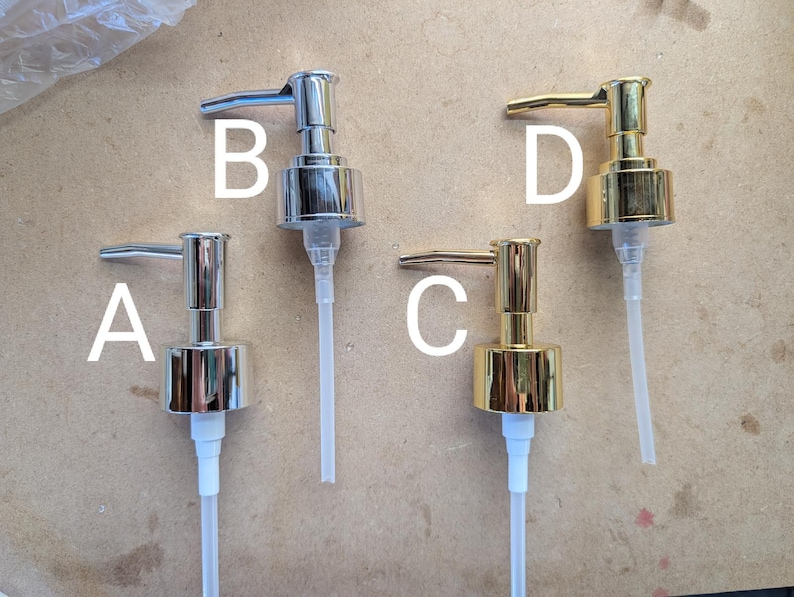 May include: Four metal soap dispenser pumps in silver and gold tones. Two are silver, labeled A and B, and two are gold, labeled C and D. Each pump has a long, clear plastic tube for dispensing liquid. The pumps are designed for use with soap or lotion bottles.