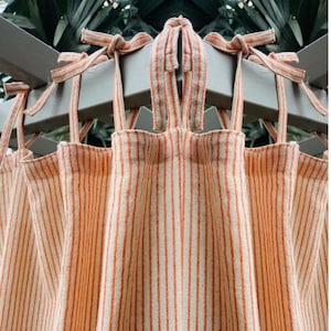 May include: A pair of orange and white striped curtains with ties at the top. The curtains are made of a lightweight fabric and have a relaxed, casual look. The text "WARMTHWONDER" is visible at the bottom of the image.