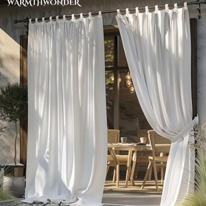 May include: White sheer curtains with a rod and rings hanging in a doorway. The curtains are tied back on each side. The curtains are in front of a patio with a table and chairs.