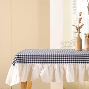 May include: A navy blue and white checkered tablecloth with a white ruffled edge. The tablecloth is draped over a wooden table. The text "Warmth Wonder" is visible on the table.