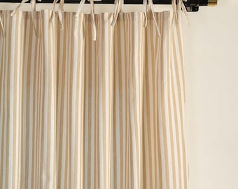 May include: Beige and white striped curtain panels hanging from a black rod with gold accents. The curtains are tied to the rod with cream-colored fabric ties. The vertical stripes create a classic, neutral look.