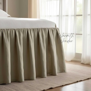 Könnte beinhalten: Ein beigefarbener Bettrand mit einem plissierten Design, der die Basis eines Bettes bedeckt. Das Bett ist mit einer weißen Tagesdecke bedeckt. Der Text "Warmth Wonder" ist auf der rechten Seite des Bildes sichtbar. Das Bett steht auf einem beigen Teppich.