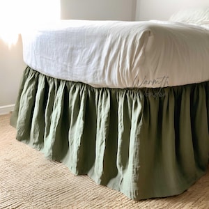 May include: A sage green bed skirt with a ruffled design. The bed skirt is made of a soft, textured fabric and is draped around the base of a bed with a white sheet and comforter. The text "Warmth Wonders" is visible.