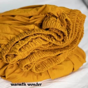 May include: A mustard yellow fitted sheet with elastic all around the edges. The sheet is folded and bunched up, showing the elastic detail.