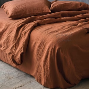 May include: A rust-colored linen bedding set with a flat sheet, fitted sheet, and two pillowcases. The bedding is made of 100% linen and is soft and breathable.