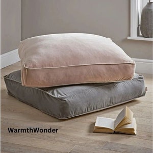 May include: Two floor cushions, one light pink and one gray, stacked on top of each other. The cushions are made of a soft, plush fabric and have a simple, rectangular shape.