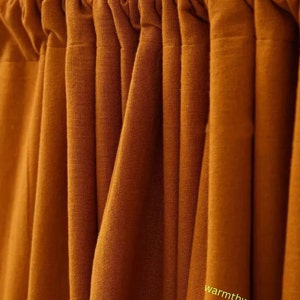 May include: Close-up of a set of rust-coloured curtains with a gathered top. The curtains are made of a soft, textured fabric.