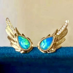 Può includere: Un paio di orecchini d'oro con una pietra di opale a forma di lacrima e dettagli di diamanti. Gli orecchini hanno la forma di ali.