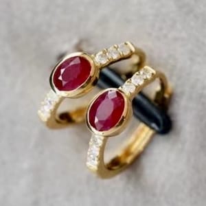 Può includere: Un paio di orecchini a cerchio in oro con una pietra preziosa di rubino rosso e una fila di diamanti trasparenti su ogni cerchio.