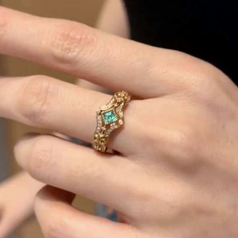 May include: A gold ring with a green gemstone surrounded by smaller diamonds. The ring has a delicate, ornate design.