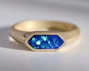 May include: A gold ring with a blue opal gemstone set in a hexagonal bezel. The ring has a textured band and a small diamond accent.