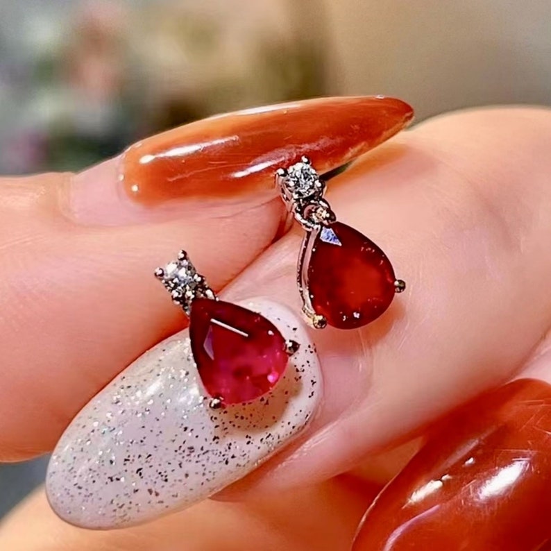 Pu&ograve; includere: Un paio di orecchini d'argento con una pietra preziosa di rubino a forma di lacrima e un piccolo accento di diamante.