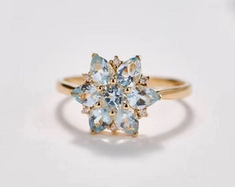 May include: A gold ring with a flower-shaped design featuring a cluster of light blue aquamarine gemstones surrounded by smaller diamonds.