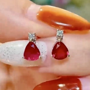 Pu&ograve; includere: Un paio di orecchini d'argento con pietre preziose rosse a forma di goccia e piccoli accenti di zircone cubico trasparente.
