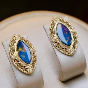 Può includere: Un paio di orecchini d'oro con una pietra preziosa di opale blu e verde incastonata in un design a filigrana.