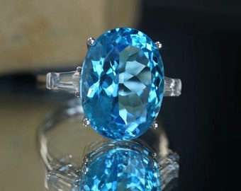 May include: A ring with a large oval-shaped blue topaz gemstone surrounded by smaller clear gemstones.